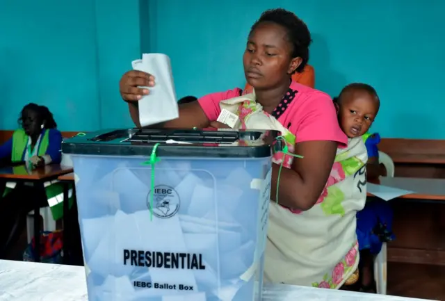 A woman is watched by a young child as she casts her vote into a ballot box at a polling station at Mutomo Primary School in Kiambu on October 26, 2017, as polls opened for the Kenyan presidential elections