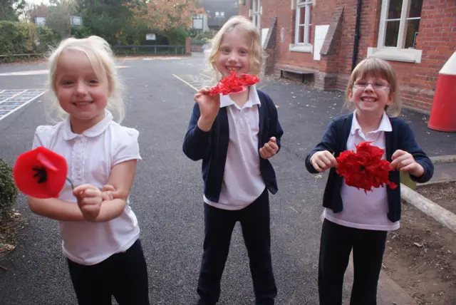 Three young schoolgirls hold up the poppies they have made