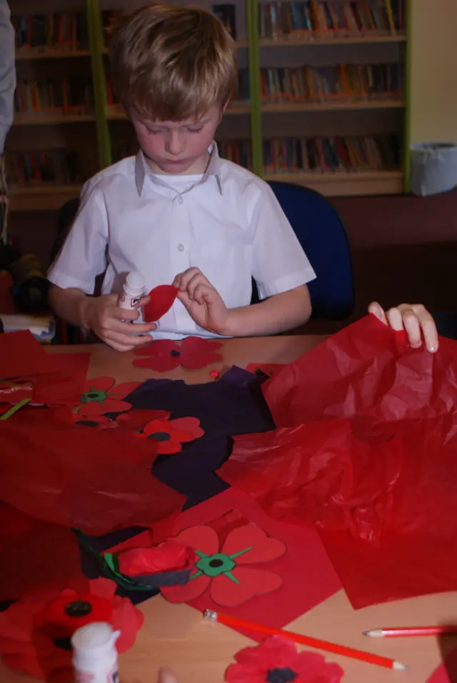 A young schoolboy with red paper, makes a poppy