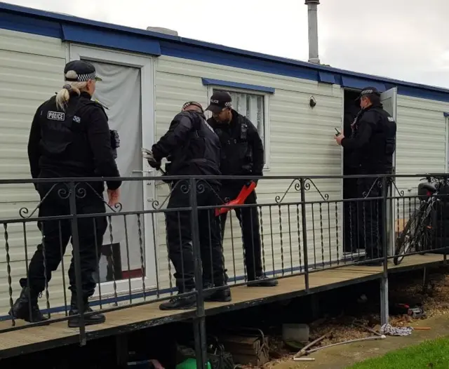 Police break open the door of a static caravan