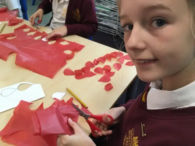 A young girl holds scissors and cuts poppy petal shapes from red tissue paper