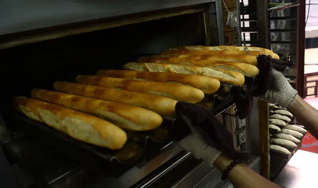 A baker takes baguettes out of the oven