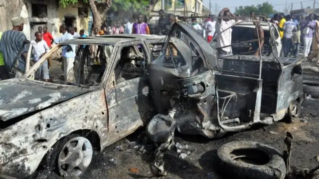 Bystanders look on at a bombed-out car