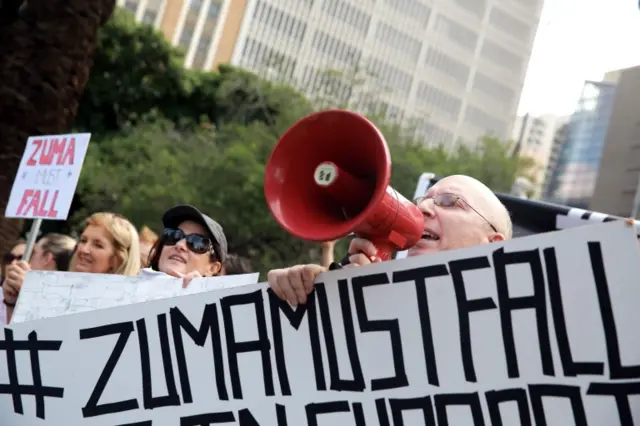 : #ZUMAMUSTFALL supporters and campaigners hold banners reading slogans against South African president Jacob Zuma as they demonstrate and shout slogans on February 11, 2016 in Durban