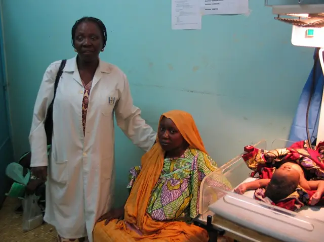 A woman sits next to her newborn child as a nurse stood by her side