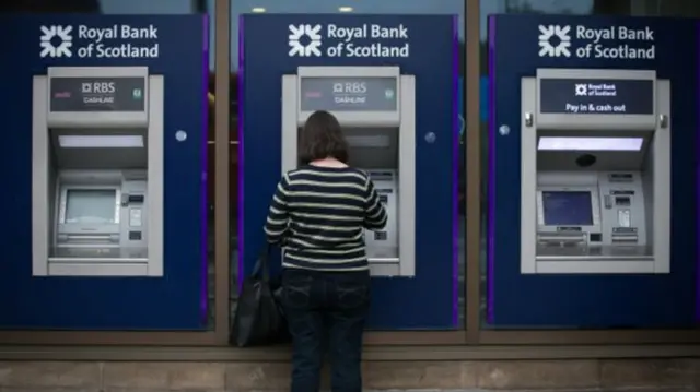 Row of bank machines with woman taking cash out