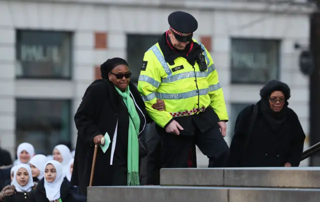 An officer helps a woman with a walking stick arrive at St Paul's Cathedral