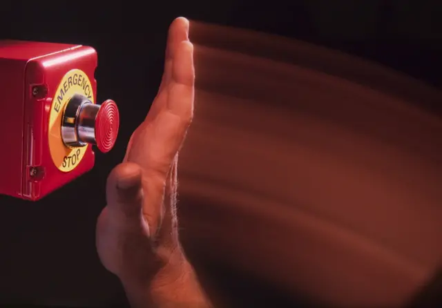 A hand pushing an emergency stop button