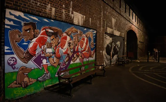 Fans walk to Gloucester rugby match past a mural of players