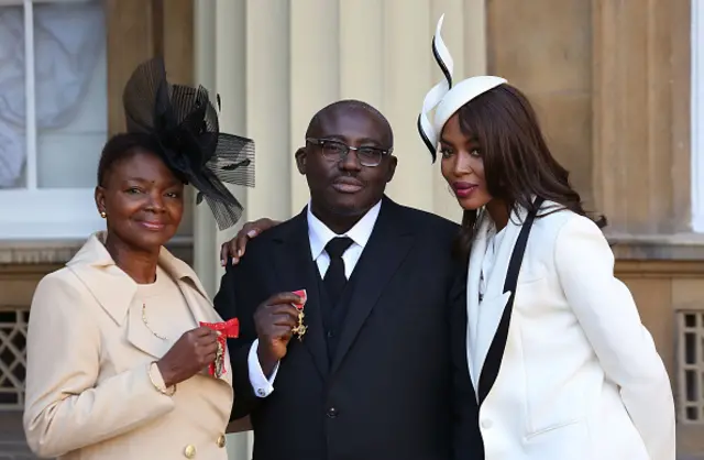 Edward Enninful (C) poses his insignia after being appointed an Officer of the Order of the British Empire (OBE) with Baroness Amos (L) and British model Naomi Campbell (R