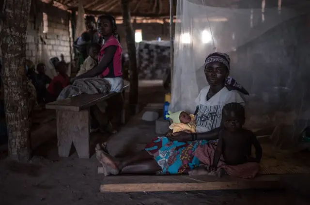 A woman sits with her baby and toddler in a dark building in the DR Congo