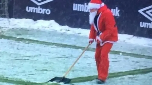 Santa shovels snow at a football match