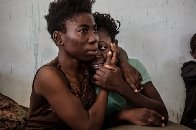 In this image released Monday Feb. 13, 2017, by World Press Photo titled "The Libyan Migrant Trap" by photographer Daniel Etter which won third prize in the Contemporary Issues, Singles, category of the World Press Photo contest shows two Nigerian refugees cry and embrace in a detention center for refugees in Surman, Libya, on 17 Aug. 2016