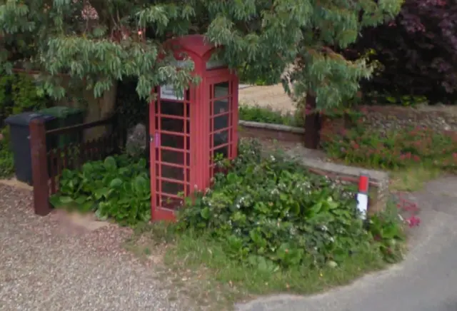 A red phone kiosk, surrounded by shrubs and flowers