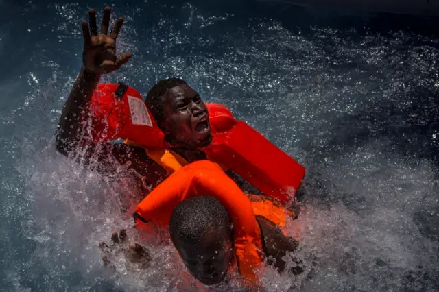 Two men panic and struggle in the water during their rescue. Their rubber boat was in distress and deflating quickly on one side, tipping many migrants in the water. They were quickly reached by rescue swimmers and brought to safety