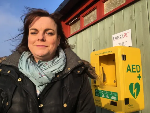 Jayne Biggs standing by the broken defibrillator box