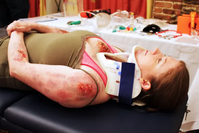 Woman in neck brace, with injuries to arm, lying on a hospital trolley - for training purposes at the QEH