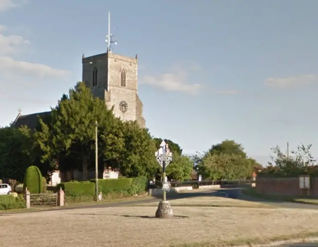 Caston church with the village sign in the foreground