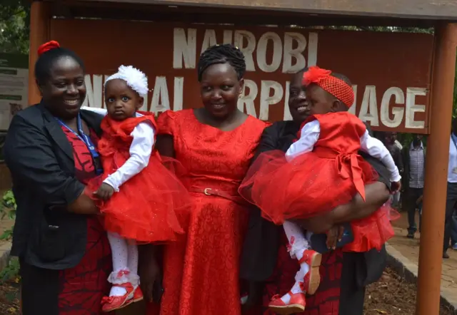 Twins are held by two nurses with their mother standing in the middle