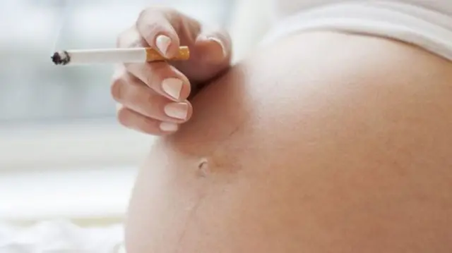 Cigarette held next to pregnant belly