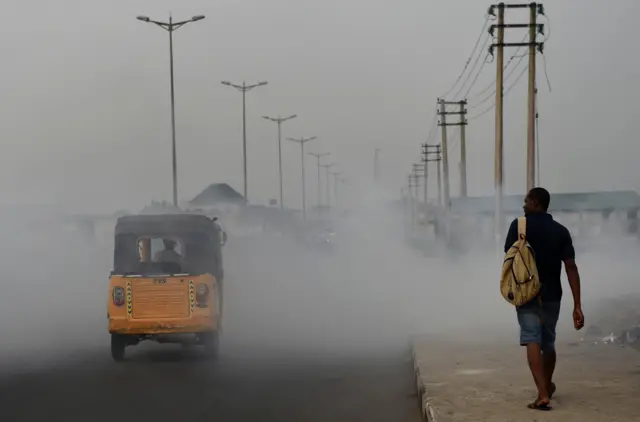 A man walks past smoke emitted from a dump in the city of Port Harcourt