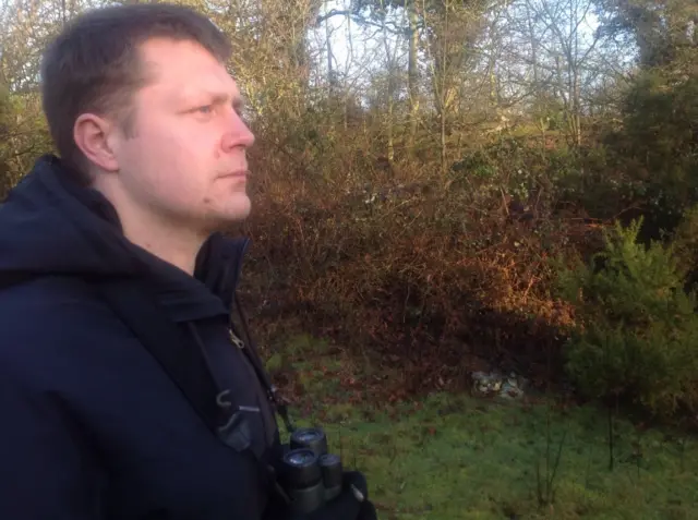 Joe Harkness, with binoculars, in a woodland setting