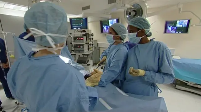 Hospital staff, in blue gowns and wearing masks, in an operating theatre