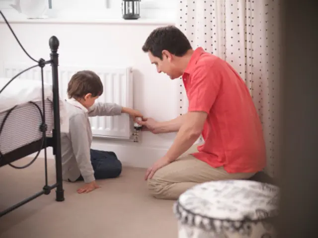 Father teaching son to adjust thermostat on radiator in bedroom of energy efficient house