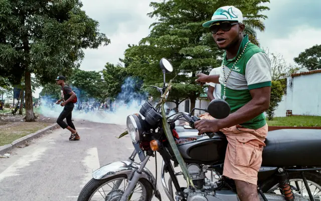 moto-taxi driver reacts as riot police fire teargas towards anti-government protesters gathered to mourn in the neighborhood of veteran Congolese opposition leader Etienne Tshisekedi of the UDPS in DRC's capital Kinshasa