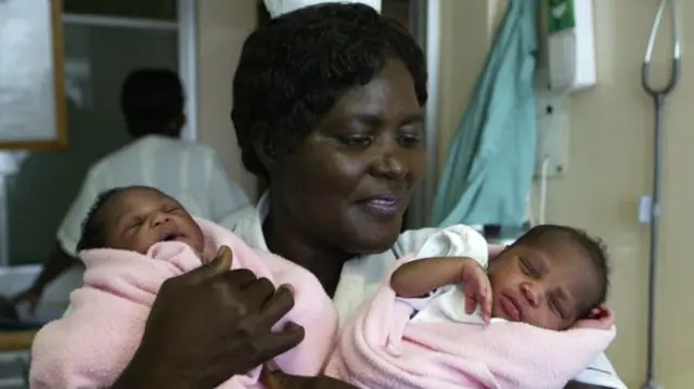 Nurse holds two newborn babies in pink swaddling