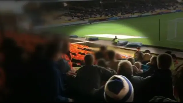 A crowd in a football stadium with a figure blurred out