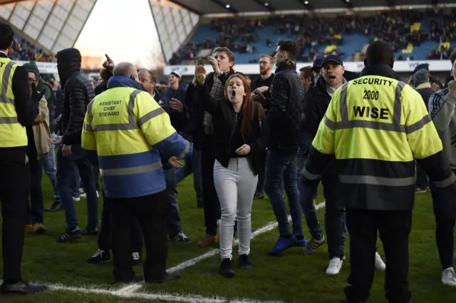 Stewards and Millwall fans on the pitch after the match