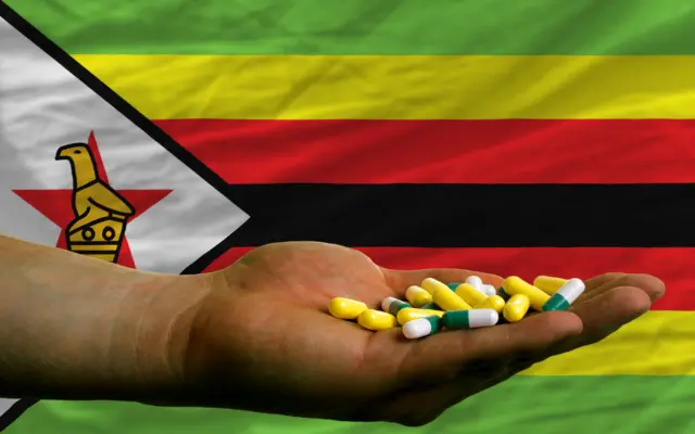 A hand with pills in front of the Zimbabwe flag