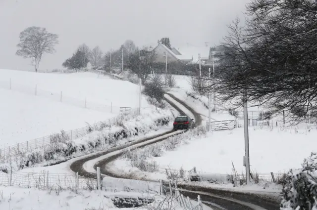 A car makes its way along a snow-covered route in Denny