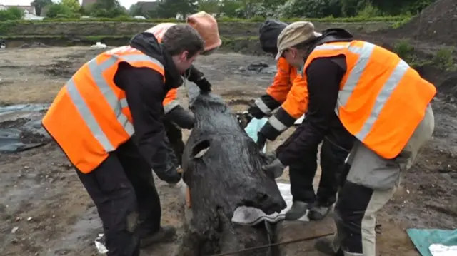 Four archaeologists lifting a wooden coffin from mud