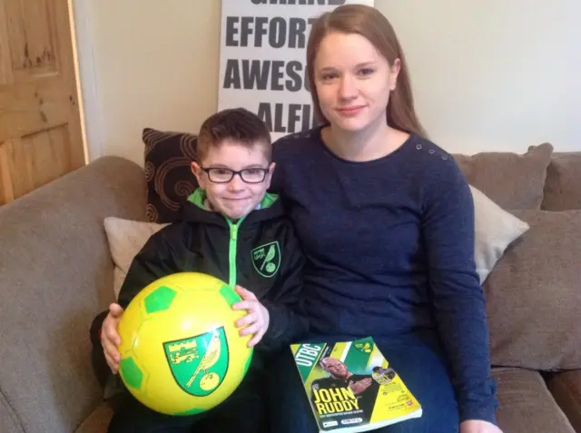 
          Alfie Oswick holding a Norwich City football, and his mum, sitting on a settee
        