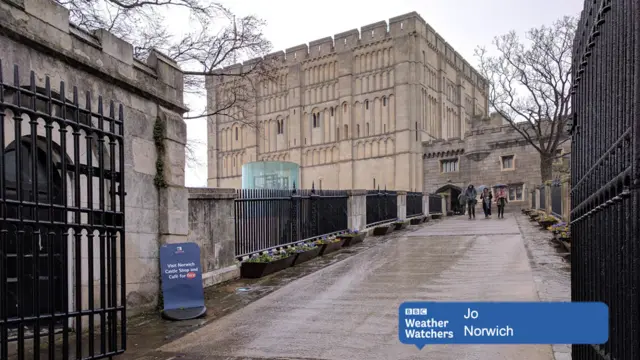 
          Norwich Castle, with a small group of people holding umbrellas
        