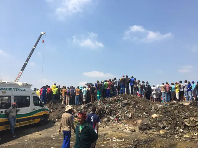 Groups of locals crowd around the open mineshaft.