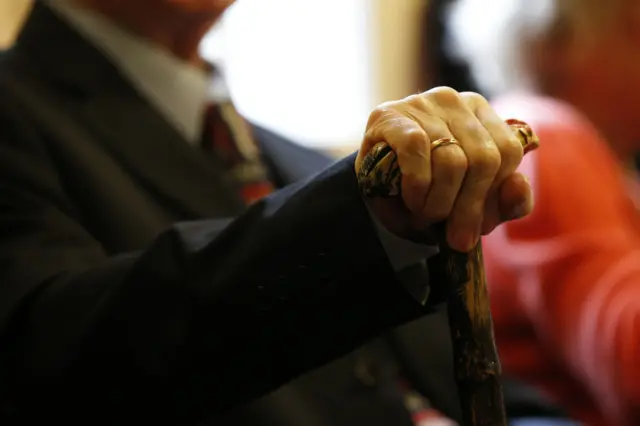 An elderly man's hands holding a walking stick