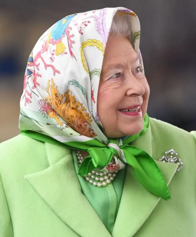 A close up image of the Queen in lime green coat, wearing pearls and a decorated headscarf