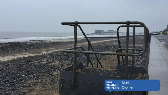 A wet and murky view of the beach and seat Cromer, with pier in background