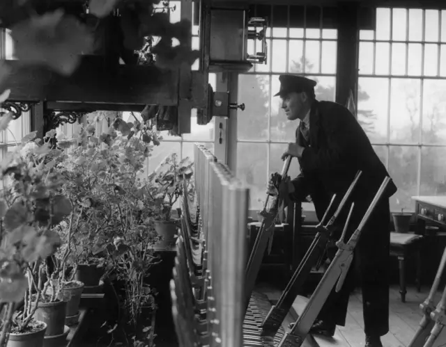 Black and white photo of signalman in signal box, with flower cuttings in pots