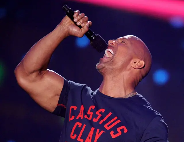 Dwayne Johnson, in blue tee-shirt bearing Cassius Clay slogan