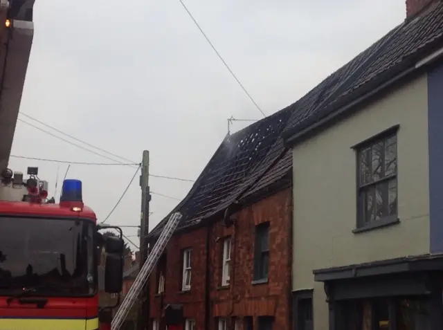 A fire engine at incident scene, with ladder reaching up to smouldering roof