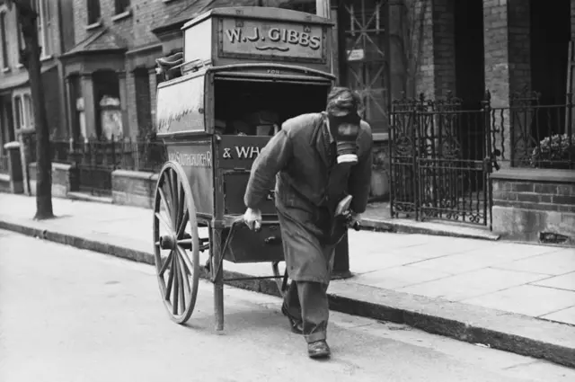 
          A baker's roundsman delivering bread while wearing his gas mask, during a gas drill in Southend-on-Sea, Essex, 29 March 1941.
        