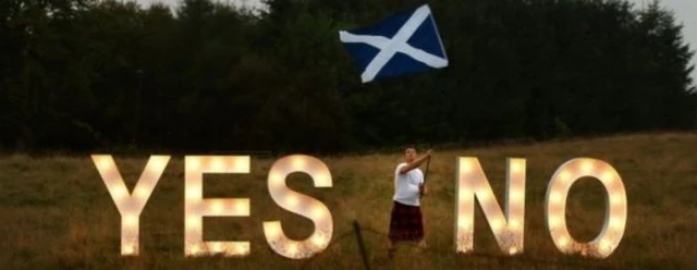 Yes and No signs with man waving Saltire flag between them