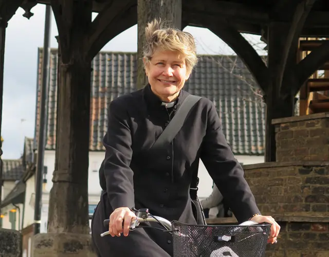 
          Revd Catherine Relf-Pennington, on a bicycle by the town's Market Cross
        