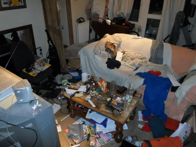 
          A room inside the property, showing drug-related paraphernalia, clothing on furniture, magazines on floor
        