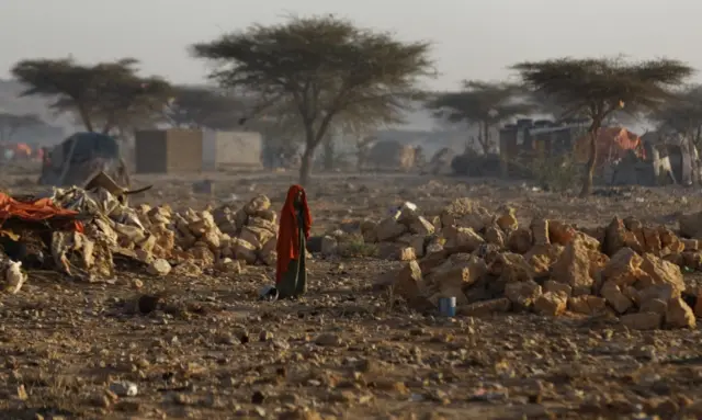 
          A Somali woman walks through a camp of people displaced from their homes elsewhere in the country by the drought, shortly after dawn in Qardho, Somalia Thursday, March 9, 2017.
        