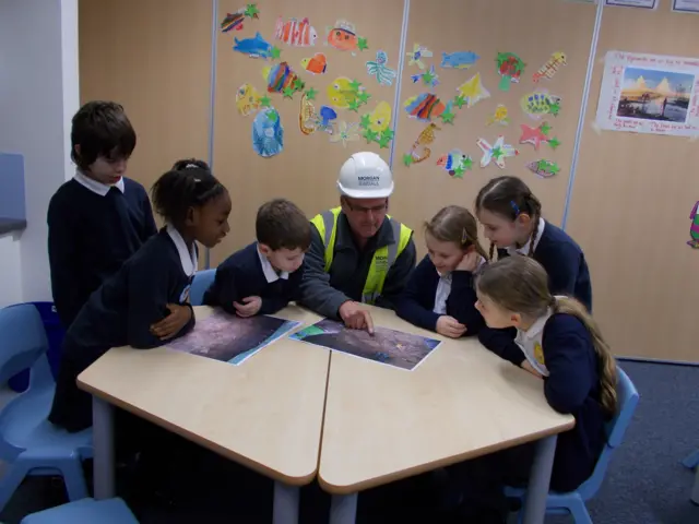 
          School pupils and a construction working sitting around a desk looking at a photo of the skeleton
        